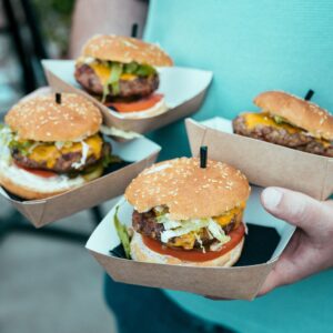 A close-up of hands holding four juicy beef burgers in cardboard trays, ideal for food lovers.